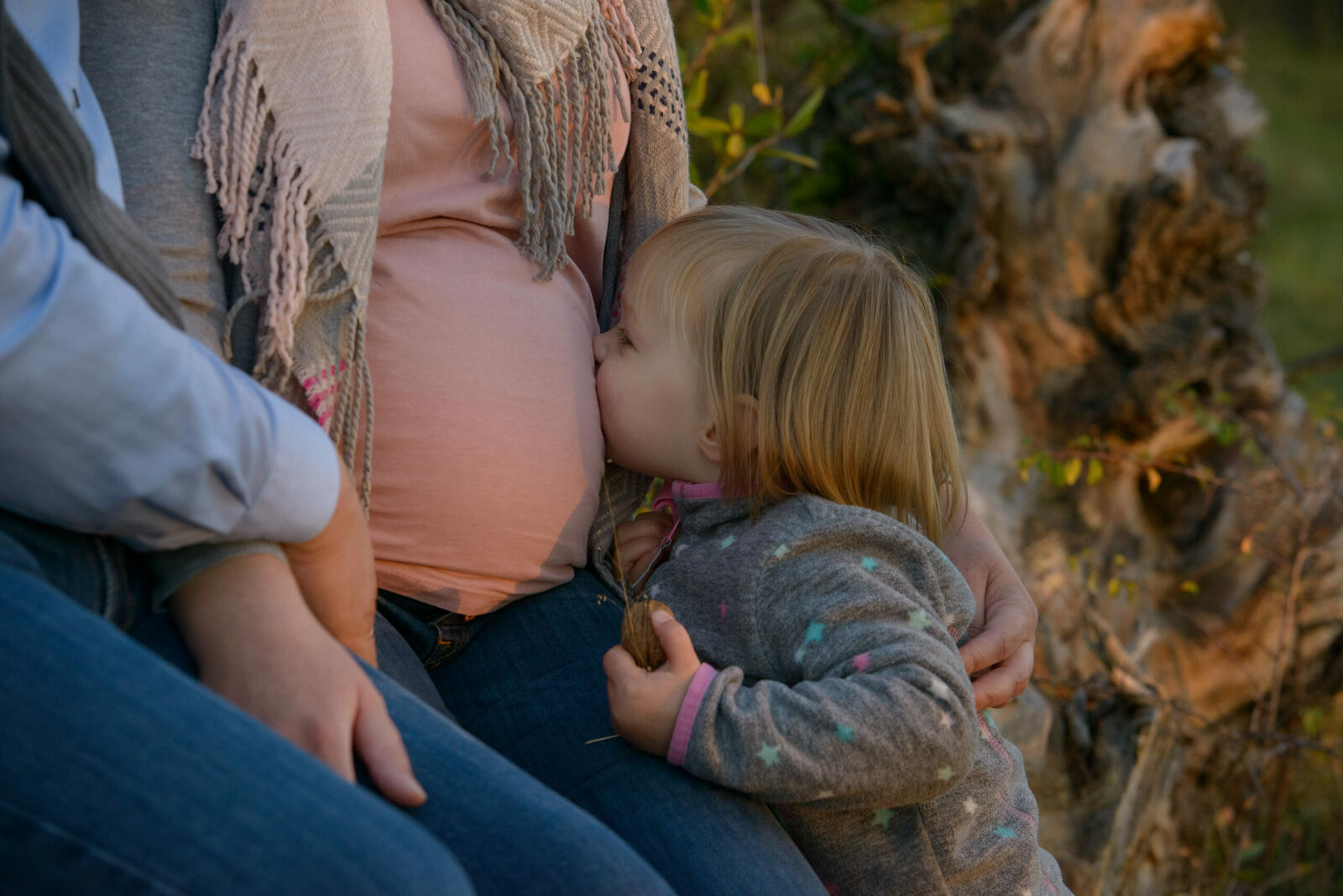 große Schwester küsst Bauch von schwangerer Mama