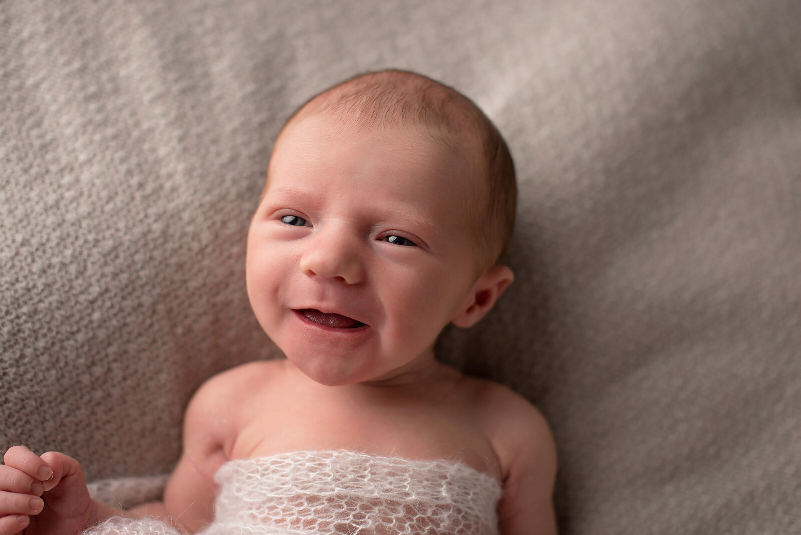 Neugeborenes Baby liegt lachend auf einer Decke