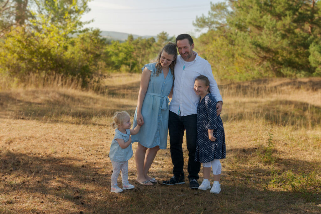 Familie als Gruppe in Sonnenuntergangstimmung steht auf einer Wiese und umarmt sich