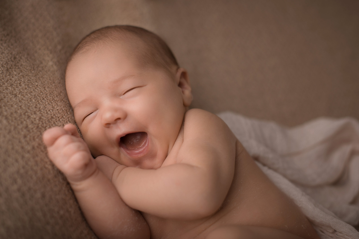 Neugeborenes Baby liegt lachend auf einer Decke