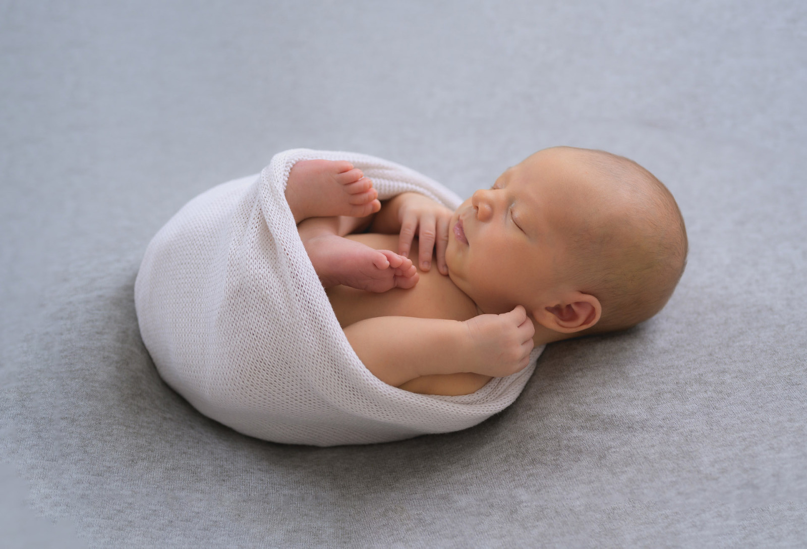 Baby in ein Tuch gewickelt liegt auf dem Rücken