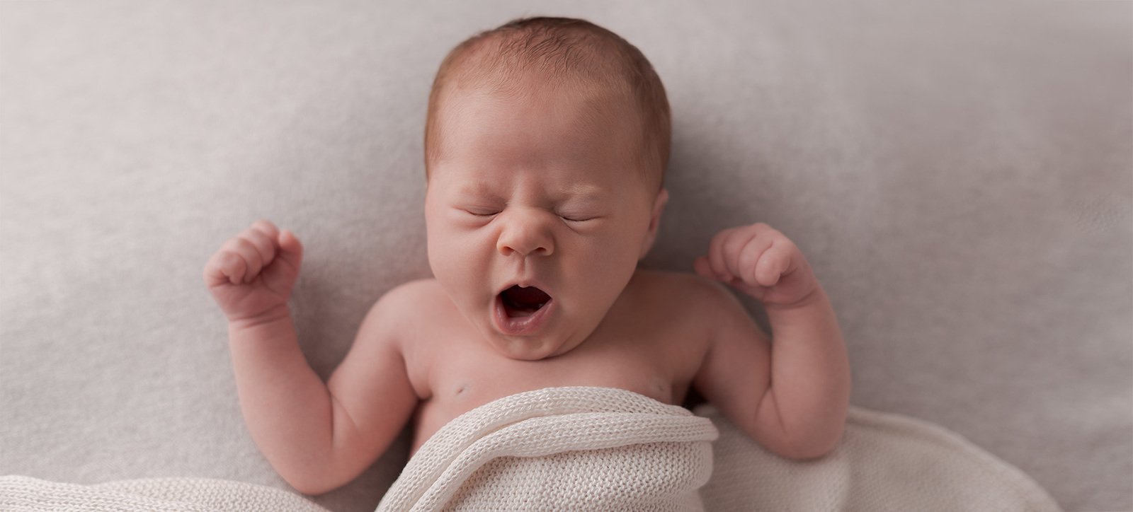 Neugeborenes Baby liegt gähnend auf einer Decke