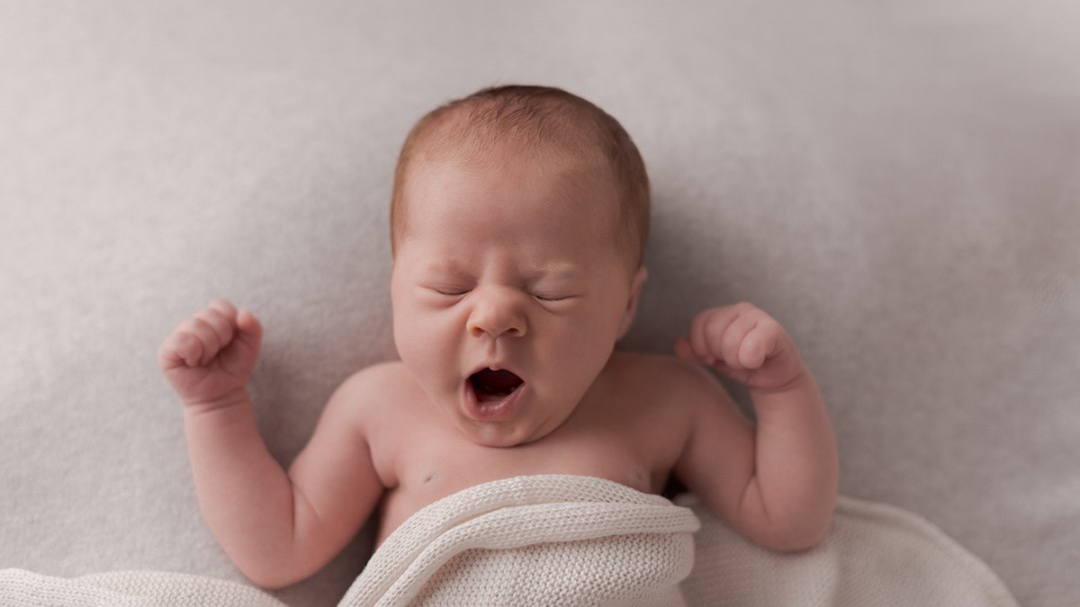Neugeborenes Baby liegt gähnend auf einer Decke
