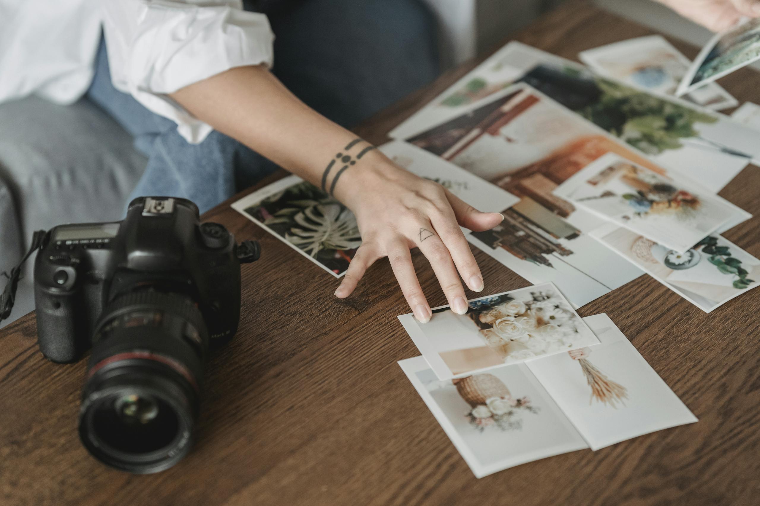 Crop unrecognizable tattooed woman picking photos of flowers at desk with professional camera in room