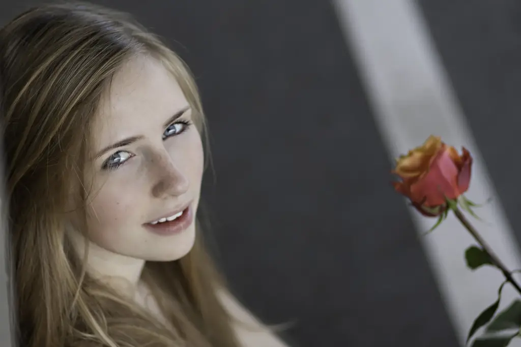 Junge Frau mit langen blonden Haaren im Profil sitzend, mit Rose in der Hand- color