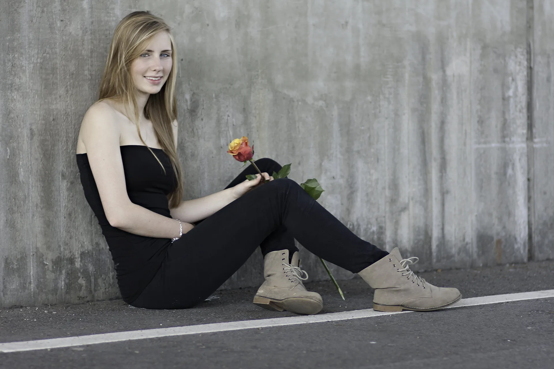 Junge Frau mit langen blonden Haaren, sitzend, Rose in der Hand, - color