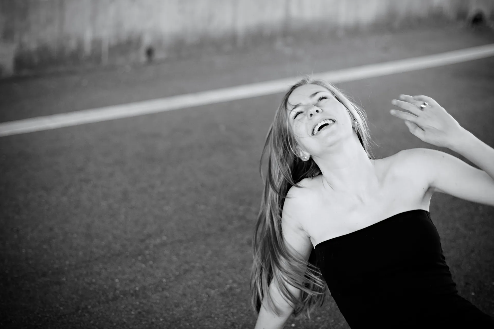 Junge Frau, sitzend auf Stra&szlig;e herzhaft lachend, schwarzes Outfit, Schwarzwei&szlig;