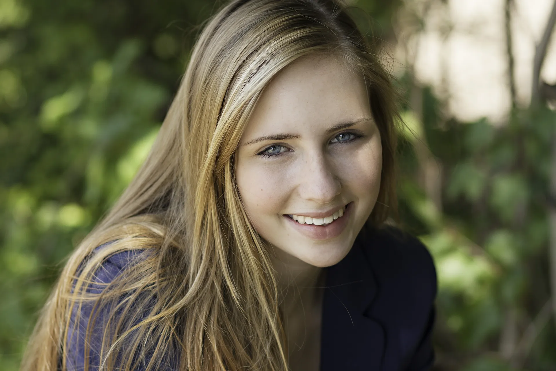 Junge Frau mit langen blonden Haaren, sitzend, sympathisch lächeld, sanftes Licht color