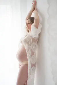 Stehende schwangere Frau tr&auml;gt Spitzen kimono H&auml;nde &uuml;ber dem Kopf helles Gegenlicht &auml;sthetisches Boudoir Portr&auml;t
