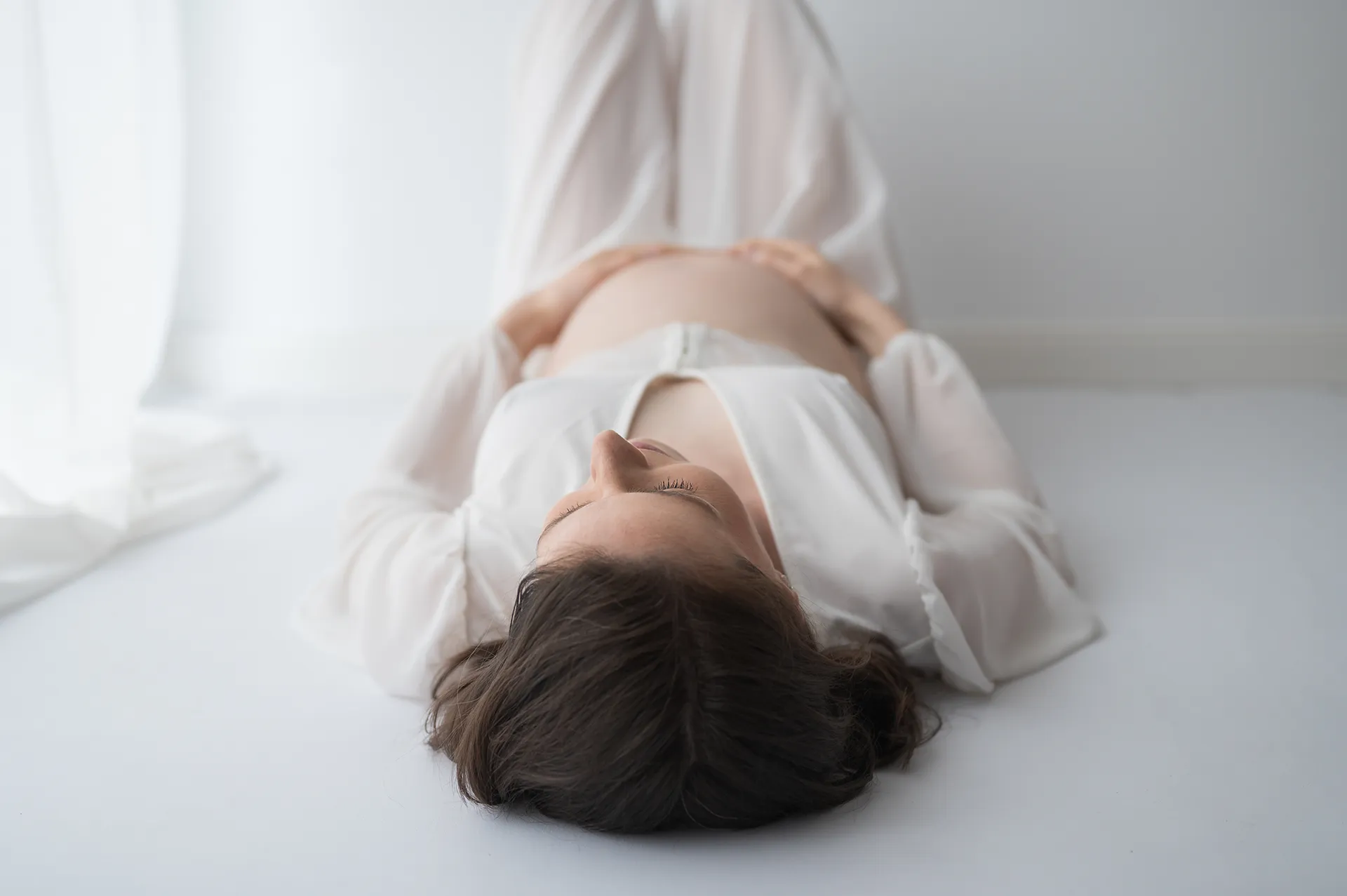 Liegende schwangere Frau fließendes Kleid Hände auf Bauch sanftes Licht elegant Color